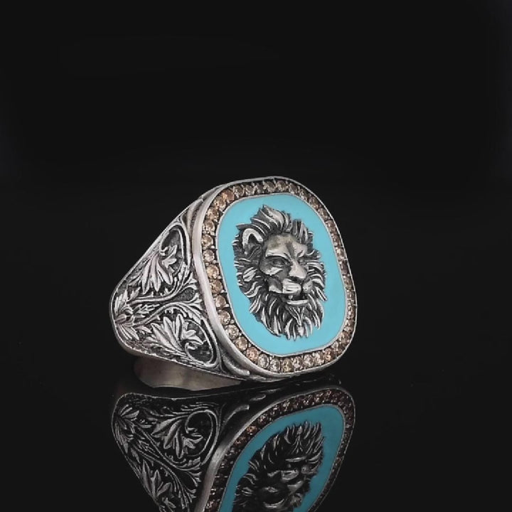Silver ring with intricate lion head design and turquoise center on a black background
